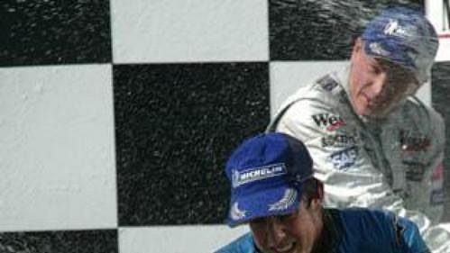 Fernando Alonso a Kimi Räikkönen (v pozadí) si užívají svůj úspěch ve Velké ceně Maďarska na stupních vítězů.