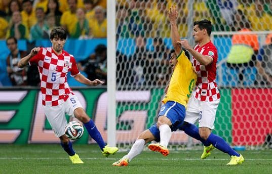 Brazilský útočník Fred (ve žlutém dresu) padá k zemi po souboji s chorvatským stoperem Dejanem Lovrenem (vpravo). Japonský sudí Nišimura následně nařídil pokutový kop pro domácí Kanárky.