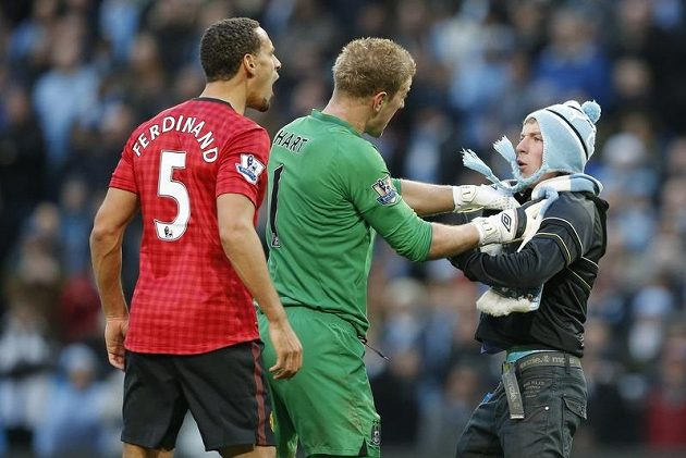 Fanouška Manchesteru City drží brankář Citizens Joe Hart (uprostřed). Vlevo obránce Manchesteru United Rio Ferdinand.
