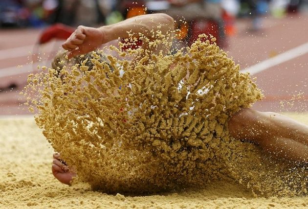 Francouzský desetibojař Kevin Mayer schovaný za závojem písku při skoku dalekém.