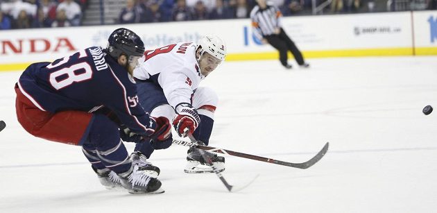 Denis Savard z Columbusu Blue Jackets odpálil puk před Dmitrijem Orlovem z Washingtonu v utkání 1. kola play off NHL.