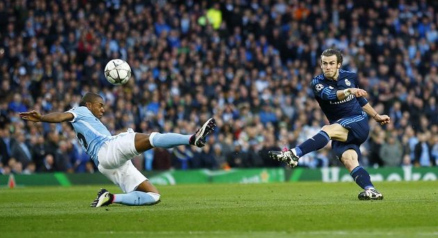 Gareth Bale střílí obávanou levačkou přes bránícího Fernandinha z týmu Manchesteru City.
