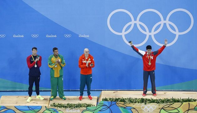 Zleva Michael Phelps, Chad Le Clos a Laszlo Cseh se tísní na stupni pro držitele stříbrné medaile. Vpravo vítěz Joseph Schooling.