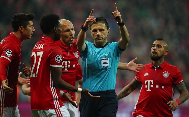 Fotbalisté Bayernu diskutují s rozhodčím po odpískaní přísné penalty ve prospěch Arsenalu.