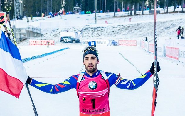 Francouzský biatlonista Martin Fourcade s vlajkou v cíli stíhacího závodu mužů ve švédském Östersundu.