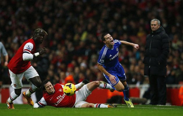 Český fotbalista Arsenalu Tomáš Rosický (ve skluzu) atakuje Cesara Azpilicuetu z Chelsea. Zcela vpravo je trenér Blues José Mourinho.