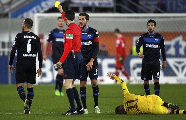 Rozhodčí Wolfgang Stark (v červeném) uděluje žlutou kartu paderbornskému Marvinu Bakalorzovi, na zemi zraněný dortmundský Marco Reus.