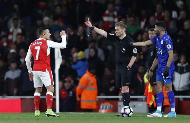 Rozhodčí Mike Jones vysvětluje útočníkovi Arsenalu, proč dostal žlutou kartu v duelu s Leicesterem. Alexis Sánchez se naopak snažil arbitra přesvědčit, že právě on byl obětí, když jej míč trefil do tváře.