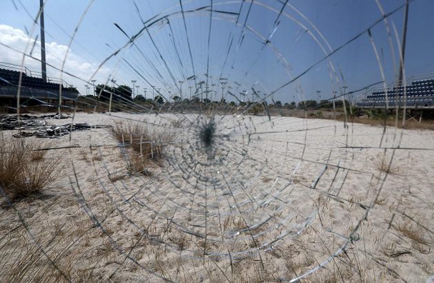 Odraz zpustošeného beachvolejbalového stadiónu v Aténách v rozbitém skle.