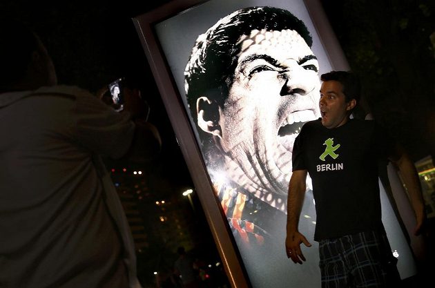 Fanoušek se fotí před reklamním billboardem, na kterém Luis Suárez cení zuby.