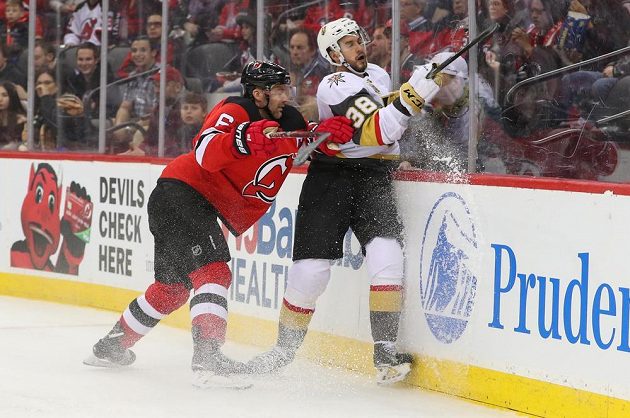 Obránce New Jersey Devils Andy Greene (6) přišpendlil českého útočníka Vegas Golden Knights Tomáše Hyku na mantinel během utkání NHL.