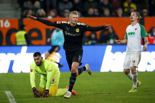 Český brankář Augsburgu Tomáš Koubek je na kolenou. Norský útočník Erling Haaland naopak slaví. V soutěžní premiéře za Dortmund třikrát skóroval.