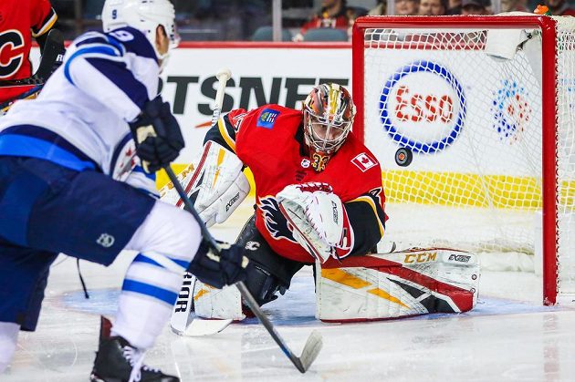 Gólman Calgary Flames David Rittich (33) v akci během utkání NHL s Winnipegem Jets. Zakončovat zkouší centr Andrew Copp (9).