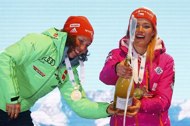 Němka Laura Dahlmeierová (vlevo) pomáhá Gabriele Koukalové při manipulaci se šampaňským na stupních vítězů po nedělní stíhačce.