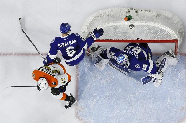 Obránce Tampy Bay Anton Stralman si puk z Gudasovy hole nešťastně sráží do vlastní branky. Vpravo je gólman Blesků Andrej Vasilevskij, vlevo útočník Letců Wayne Simmonds.
