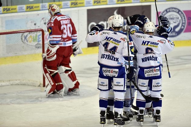 Hokejisté Komety slaví gól v síti Třince. Vlevo je zklamaný brankář Ocelářů Šimon Hrubec.