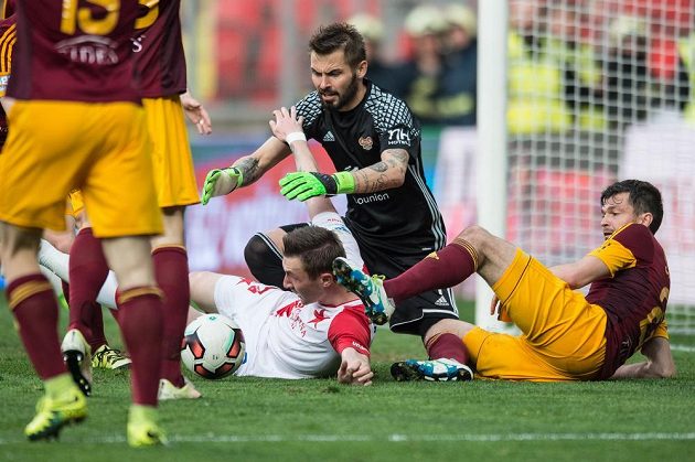 Brankář Dukly Praha Filip Rada se vrhá po míči, vedle něj je na zemi obránce Dukly Jan Šimůnek, gólmanovi brání Jaromír Zmrhal ze Slavie. Derby v Edenu skončilo 2:2.