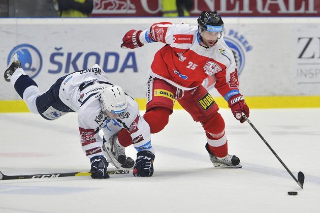 Plzeňský hokejista Vojtěch Němec padá na ledovou plochu, Zbyněk Irgl z Olomouce míří za pukem během čtvrtfinále play off hokejové extraligy.