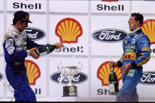 Damon Hill (vlevo) sprchuje šampaňským Michaela Schumachera po Velké ceně Brazílie v roce 1994. Po kolizi v posledním závodu sezóny by si oba spíš vjeli do vlasů.
