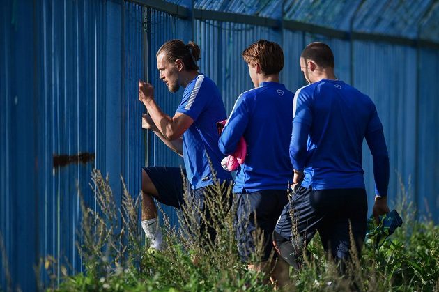Liberecký obránce Ondřej Švejdík (vlevo) a jeho spoluhráči přichází dírou v plotě na trénikové hřiště před zápasem 1. kola základní skupiny EL proti Braze.