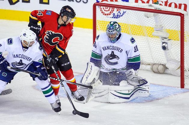 Jiří Hudler z Calgary bráněný zadákem Danem Hamhuisem se snaží prosadit před brankářem Vancouveru Ryanem Millerem.