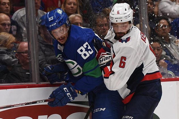 Český obránce Washingtonu Michal Kempný (v bílém) bojuje u mantinelu o puk s útočníkem Vacnouveru Jayem Beaglem během utkání NHL.