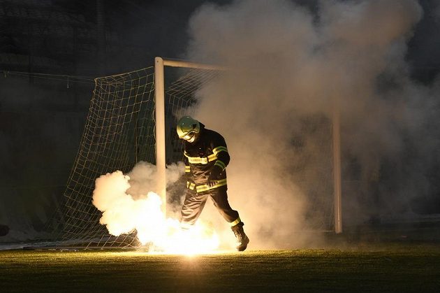 Jeden z hasičů sbírá z hřiště světlice, které tam v úvodu utkání naházeli fanoušci Sparty.