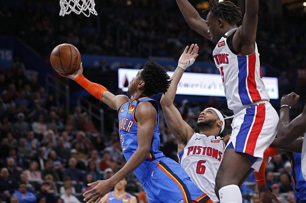 Hráč Oklahomy Shai Gilgeous-Alexander (vlevo) střílí na koš a je bráněn dvěma hráči Detroitu.