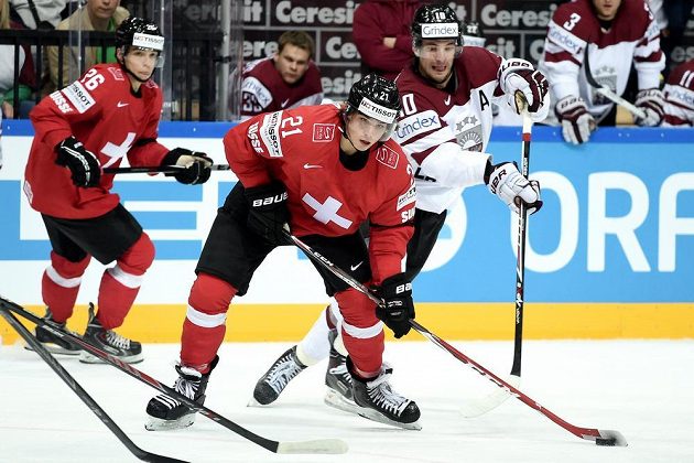 Švýcarský útočník Kevin Fiala (uprostřed) bráněný lotyšským útočníkem Laurisem Darzinsem během utkání hokejového mistrovství světa v Praze.