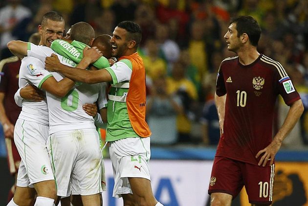 Fotbalisté Alžírska si vychutnávají postup do osmifinále MS, poprvé v historii dosáhli hráči afrického státu takového úspěchu. Vpravo je zklamaný Rus Alan Dzagojev.