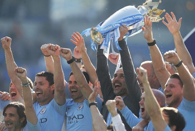 Je to doma. Manchester City slaví mistrovský titul. S trofejí si užívá manažer Pep Guardiola s hráči.