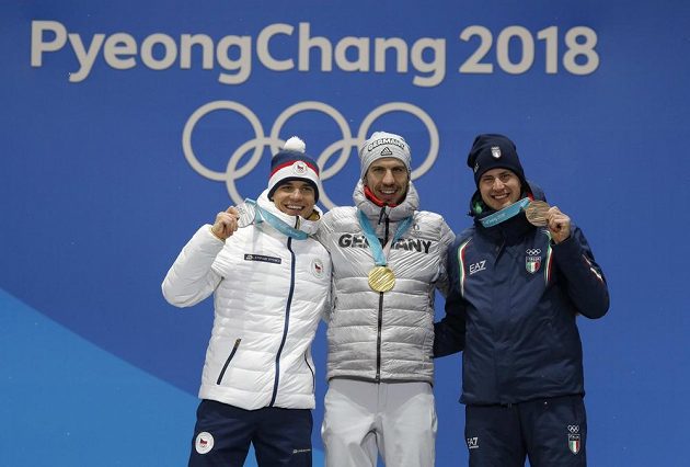 Medailový ceremoniál pro tři nejrychlejší biatlonisty z nedělního sprintu: Zlatý Arnd Peiffer (uprostřed), stříbrný Michal Krčmář (vlevo) a bronzový Dominik Windisch.