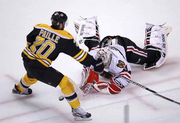 Gólman Chicaga Corey Crawford odehrává v akrobatické pozici puk před Danielem Paillem z Bostonu.