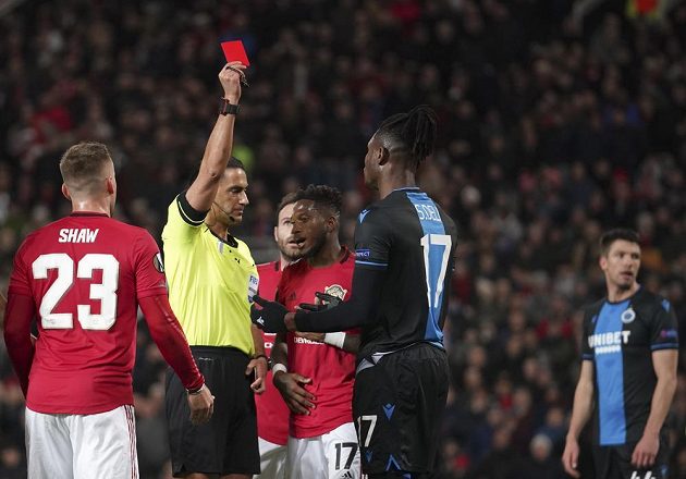 Rozhodčí Serdar Gozubuyuk dává žlutou kartu Simonu Delimu z Brugg v odvetě s Manchesterem United.
