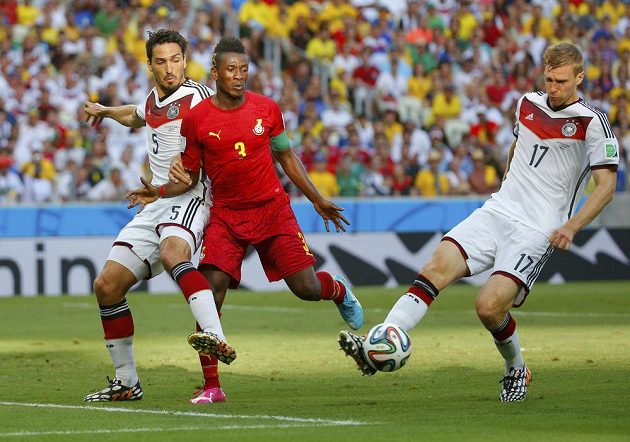 Asamoah Gyan z Ghany (uprostřed) dotírá na německého obránce Pera Mertesackera, který se pokouší uklidit míč do bezpečí.