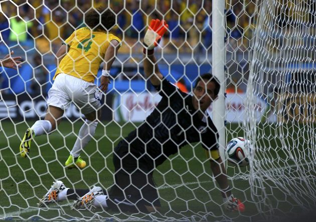 Brankář Chile Claudio Bravo loví míč ze sítě, zatímco Brazilec David Luiz běží slavit vstřelený gól.