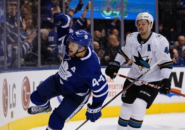 Obránce Toronta Morgan Rielly (44) slaví vítězný gól v zápase NHL se San Jose. Český útočník Sharks Tomáš Hertl vzadu smutně přihlíží.