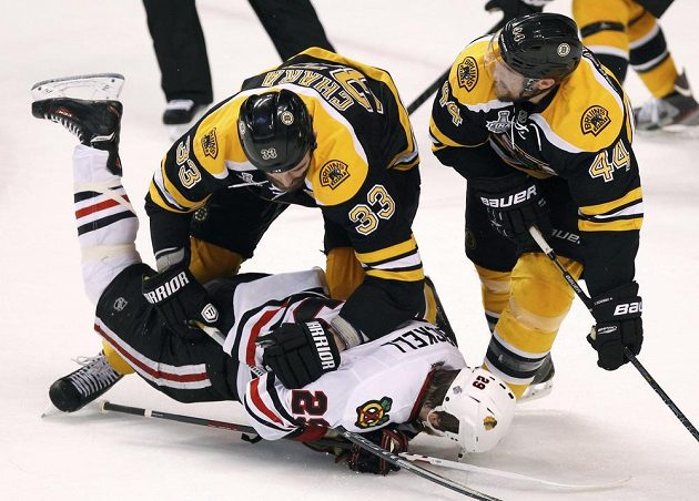 Obránce Bostonu Zdeno Chára (s číslem 33) posílá na led útočníka Chicaga Bryana Bickella. Vpravo přihlíží zadák Bruins Dennis Seidenberg.