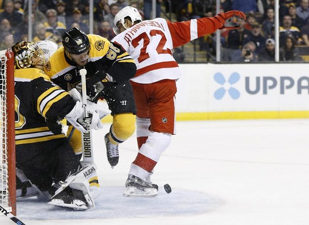 Útočník Bostonu David Pastrňák se snaží zastavit v utkání NHL útočícího Andrease Athanasiou a pomáhá tak brankáři Bruins.