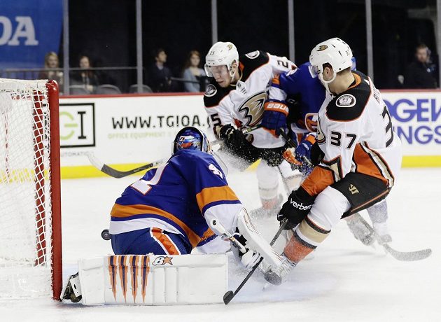 Český útočník Ondřej Kaše z Anaheimu Ducks se v utkání NHL snaží vyzrát na slovenského gólmana New Yorku Islanders Jaroslava Haláka. S číslem 37 všemu přihlíží Nick Ritchie z týmu Ducks.