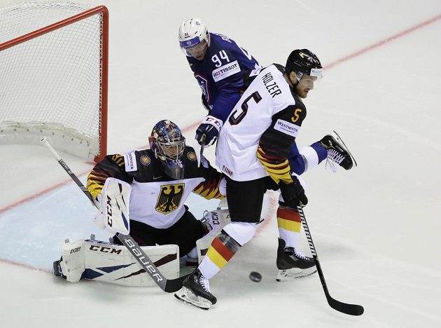 Brankář německé hokejové reprezentace Philipp Grubauer a obránce Korbinian Holzer se snaží zastavit puk mířící na německou branku. Vše sleduje Francouz Tim Bozon.