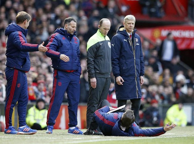 Kouč Manchesteru United Louis van Gaal leží před trenérem Arsenalu Arsénem Wengerem (vpravo), čtvrtým rozhodčím Mikem Deanem a svým asistentem Ryanem Giggsem.