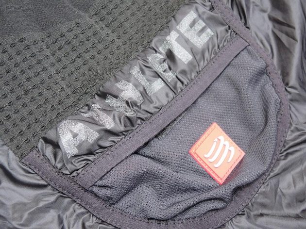 CompresSport Trail Hurricane Jacket - malá kapsa na zádech má reflexní potisk a nášivku.