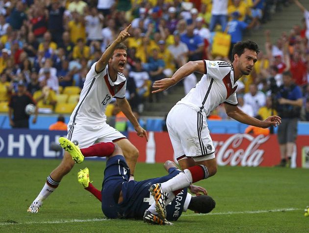 Němec Mats Hummels (vpravo) sleduje míč mířící po jeho hlavičce do sítě. Thomas Müller už jásá, Francouz Raphael Varane (na zemi) je bezmocný.