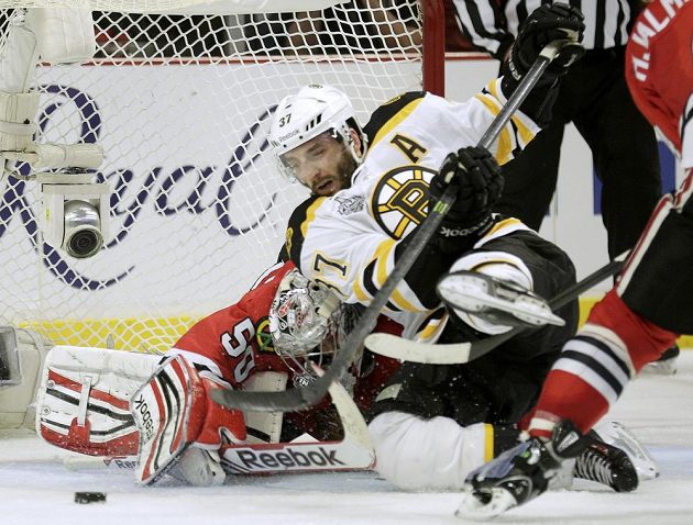 Útočník Patrice Bergeron z Bostonu padá před brankou Coreyho Crawforda z Chicaga v úvodním finále Stanley Cupu.