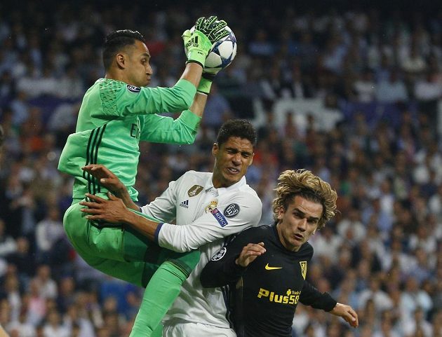 Brankář Realu Madrid Keylor Navas krotí míč v rukavicích za pomoci obránce Raphaela Varaneho. Hvězdný útočník Atlétika Antoine Griezmann se z zakončení nedostal.