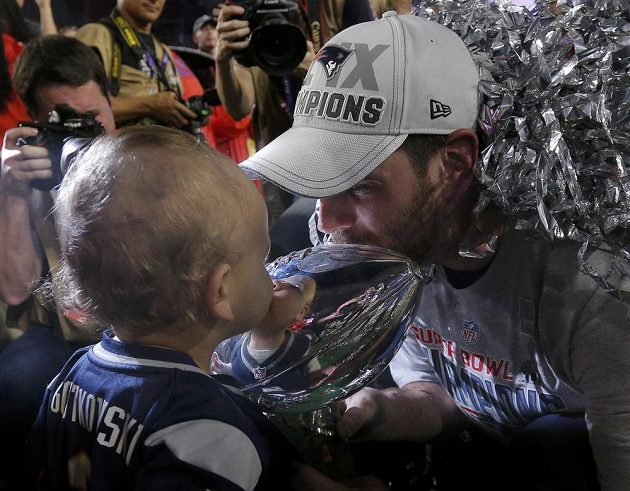 Stephen Gostkowski z vítězného týmu líbá trofej pro vítěze Super Bowlu společně se svým nejmladším synem.