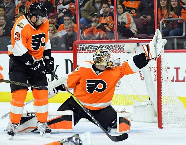 Gólman Anthony Stolarz chytá puk v utkání s Calgary, jeho zákroku přihlíží český obránce Philadelphie Radko Gudas.