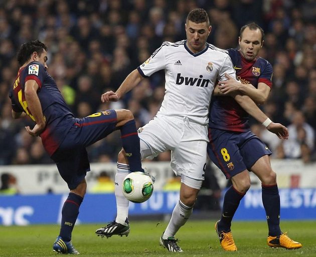 Karim Benzema z Realu Madrid bojuje s bránícími hráči Barcelony Xavim (vlevo) a Andrésem Iniestou.