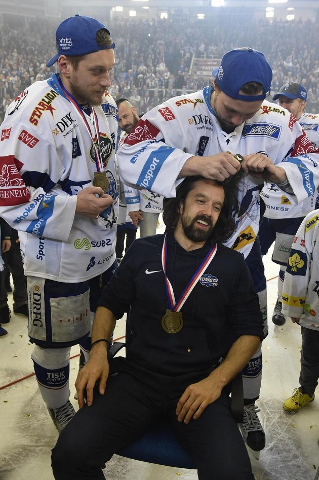 Ondřej Němec z Brna stříhá po zisku titulu kondičního trenéra Komety Miloše Pecu, který prohrál sázku. Vlevo je Marcel Haščák. Kometa Brno vyhrála hokejovou extraligu.